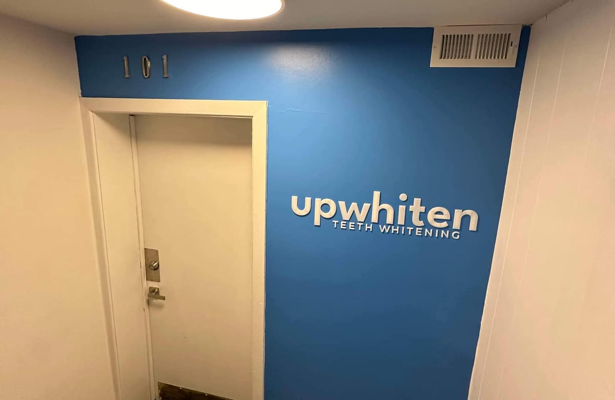 The door to Suite 101 beside the UpWhiten Teeth Whitening logo on a blue wall